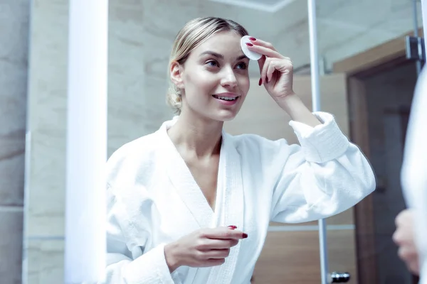 Krásná mladá žena čištění její tvář stojící před zrcadlem — Stock fotografie