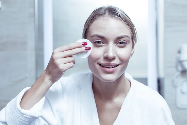 Blue-eyed good-looking woman removing makeup from face with cotton pad