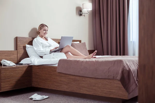 Rozpromieniony atrakcyjna kobieta pracuje na laptopie podczas leżenia w łóżku — Zdjęcie stockowe