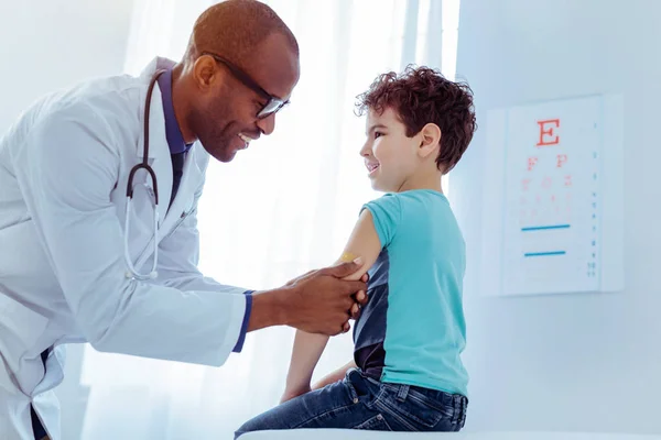 Positive nice man putting plaster on boys arm — Stock Photo, Image