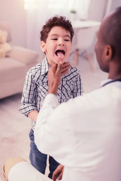 漂亮可爱的男孩显示他的舌头 而站在医生面前 — 图库照片
