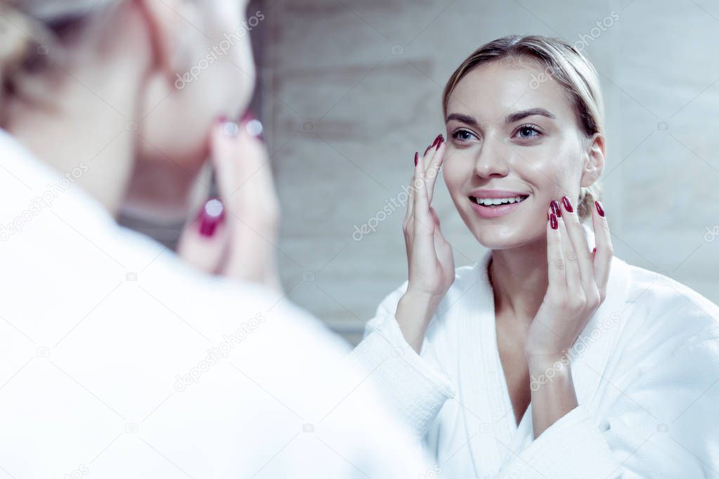 Beautiful young woman smiling while looking into mirror and using cream