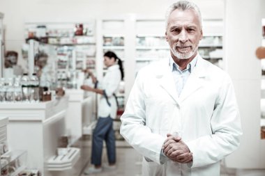 Sakallı eczacı müvekkillerine tanışmak hoş görünümlü bir beyaz palto giyiyor