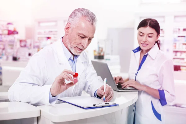 Седовласый врач осматривает контейнер с помощью лекарств — стоковое фото