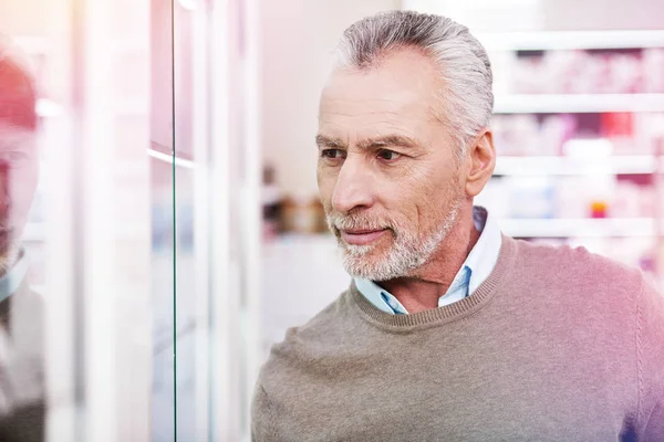 Handsome interested grey-haired man visiting a pharmacy — Stock Photo, Image