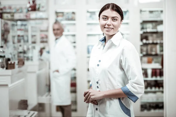 Tilltalande grönögda apotekspersonal ler medan möte klienter i apotek — Stockfoto