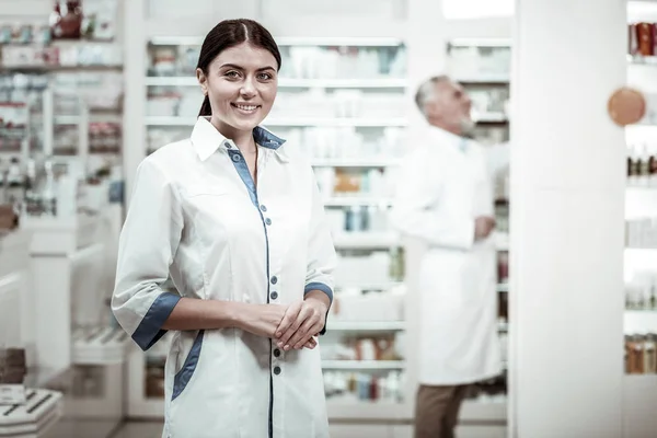 Farmacéutico de ojos verdes. Atractivo farmacéutico de ojos verdes sonriendo ampliamente mientras se reúnen con clientes en la farmacia —  Fotos de Stock