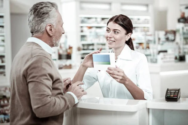Green-eyed pharmacy worker smiling while communicating with her visitor — Stock Photo, Image