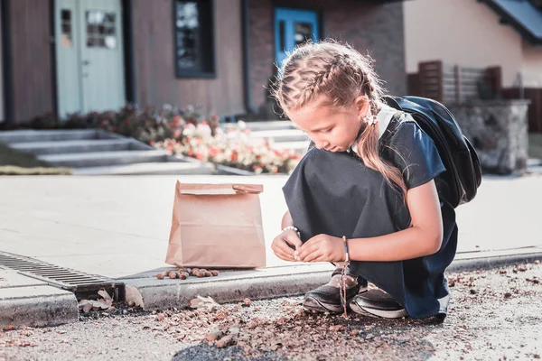 Liten skolflicka med ryggsäck tittar på kastanjer medan gå hem — Stockfoto