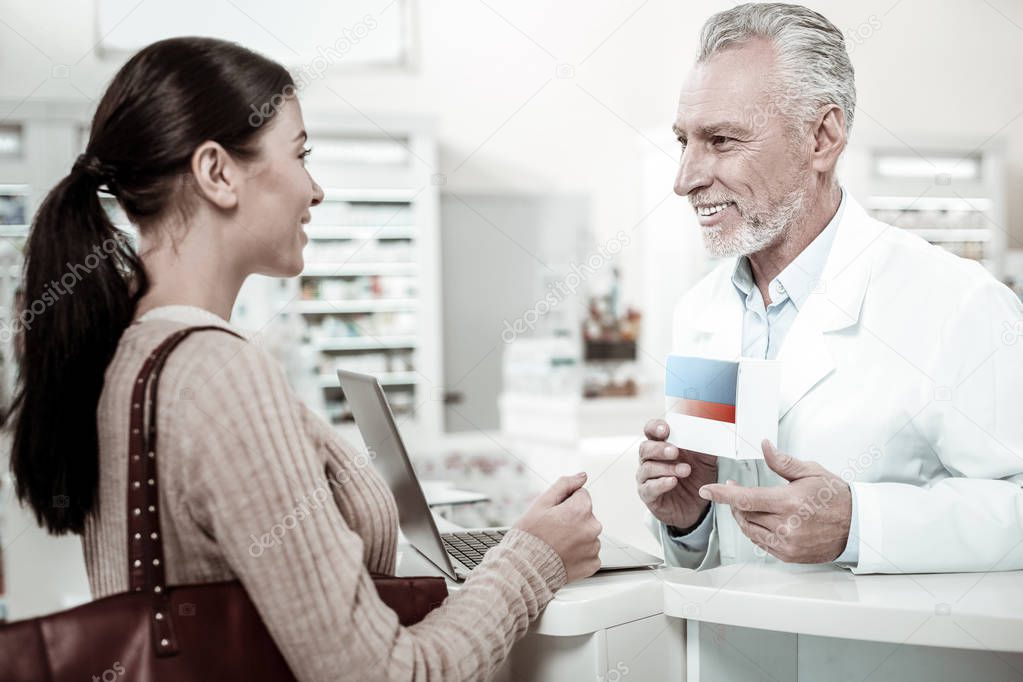 Pleasant smiling bearded pharmacist recommending good pills his visitor