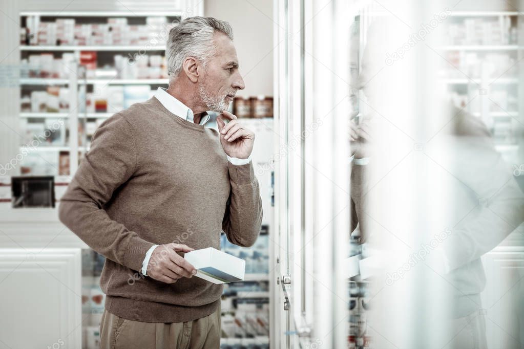 Businessman wearing brown trousers standing near glass windows in pharmacy