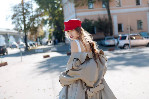 Belle femme aux yeux foncés aux lèvres rouges enlevant son manteau beige — Photo