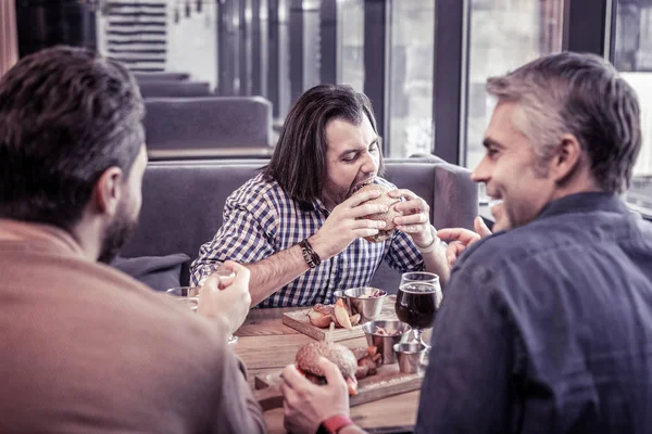 Сконцентрированный брюнетка мужчина ест бургер с удовольствием — стоковое фото