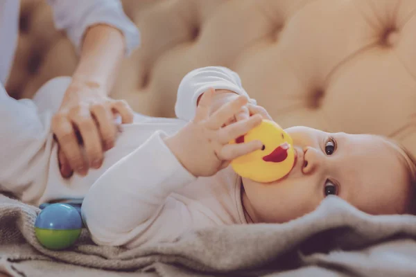 Piccola adorabile bambina che gioca con i giocattoli mentre giace vicino alla madre premurosa — Foto Stock