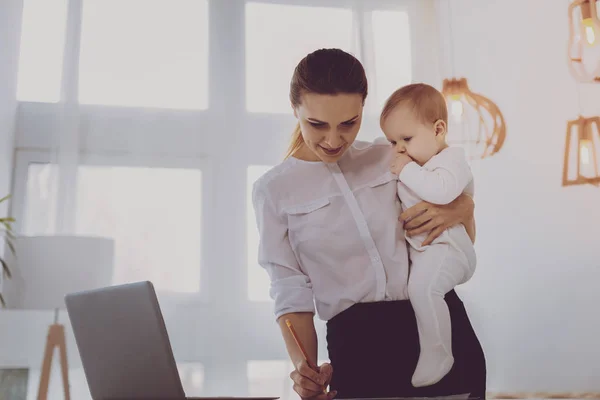 Modedesignerin im Mutterschaftsurlaub zeichnet Skizzen, während sie Baby im Arm hält — Stockfoto