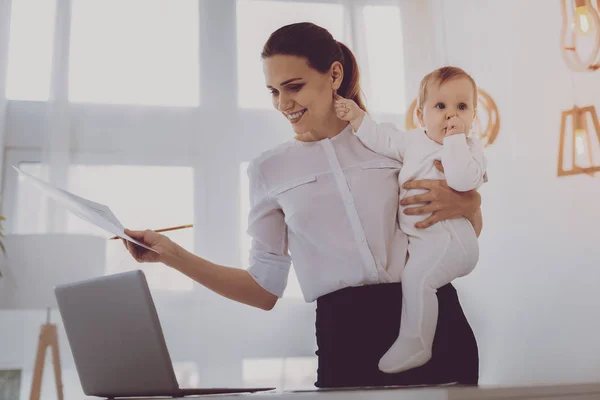 Junge berufstätige Mutter lächelt, während sie ihr kleines blondhaariges Baby stillt — Stockfoto