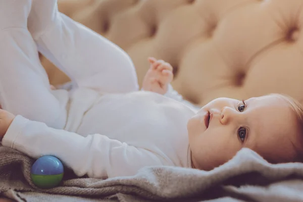 Pouco bonito de olhos azuis criança sorrindo enquanto deitado no sofá perto de babá — Fotografia de Stock