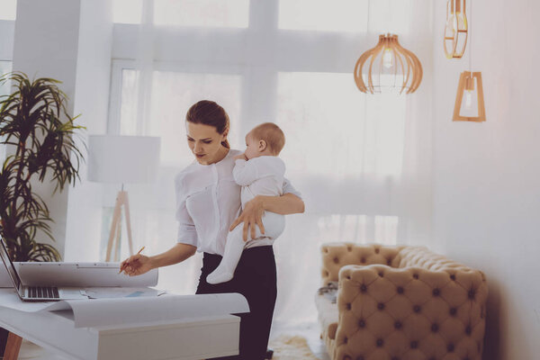 Успешная работающая мать, стоящая возле лампы в гостиной, держа дочь
