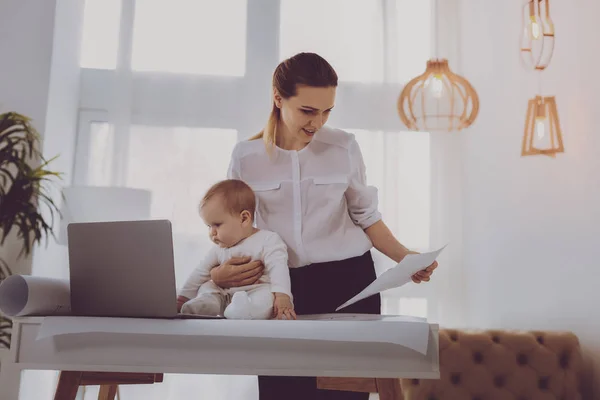 现代母亲现代母亲感到忙着把她可爱的女婴放在笔记本电脑前 而在家里工作 — 图库照片