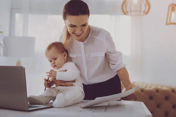 Cute adorable baby playing with pencil sitting near busy working mother — Stock Photo, Image