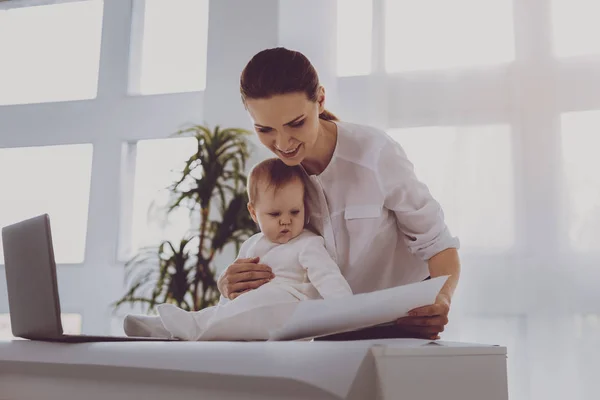 Belle mère travaillant tout en se tenant près de la plante décorative avec bébé — Photo