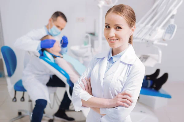 Dentista alegre sorrindo enquanto seu colega examinando o paciente — Fotografia de Stock