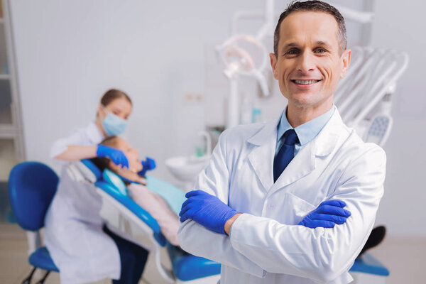 Qualified dentist standing with his arms crossed and looking happy