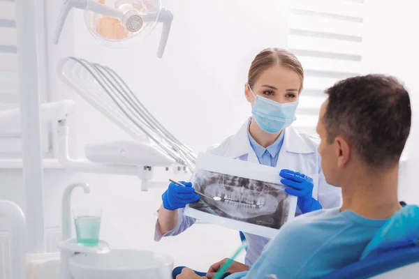 Qualified dentist holding an X ray while talking to her patient — Stock Photo, Image