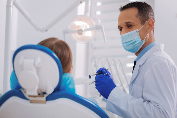 Attentive dentist listening to his patient while standing with instruments