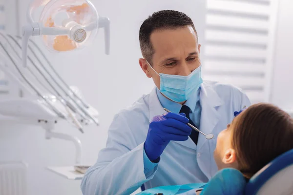 Dentista cuidadoso sosteniendo un espejo dental mientras mira los dientes —  Fotos de Stock