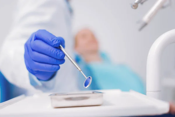 Zorgvuldige tandarts nemen een tandheelkundige spiegel terwijl u werkt — Stockfoto