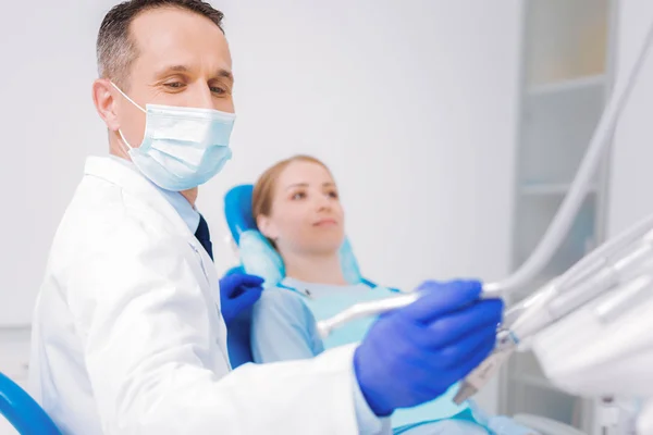 Dentiste joyeux assis près de son patient et de prendre une perceuse dentaire — Photo