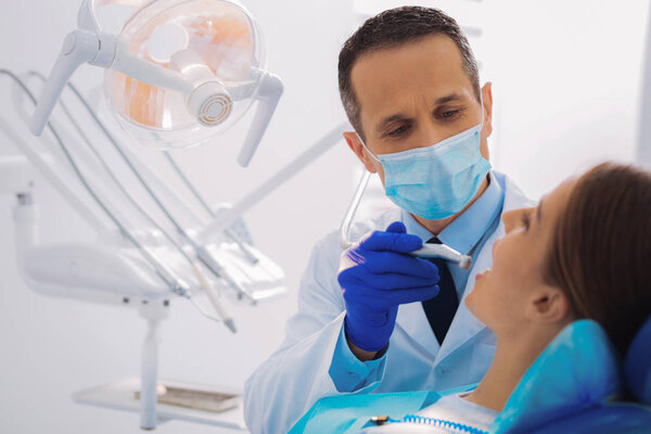 Serious doctor holding a dental drill while curing his patient