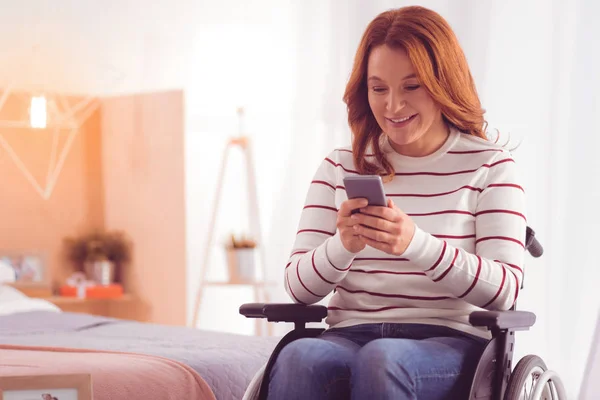Mujer con silla de ruedas positiva usando smartphone — Foto de Stock