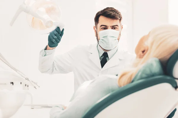 Dentista que regula a direção da luz da lâmpada dental — Fotografia de Stock