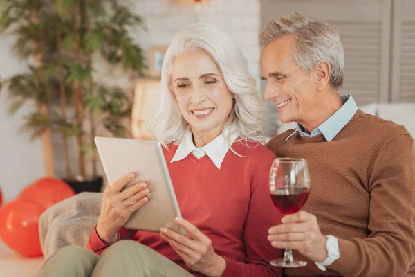 Esposos seniores satisfeitos descansando com copo de vinho e tablet — Fotografia de Stock