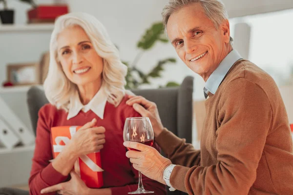 Leende äldre man med ett glas vin sitter med sin fru — Stockfoto
