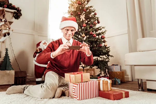 Glad trevlig man sitter och gör foto av gåvor. — Stockfoto