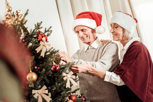 Ocupado agradable pareja de pie y la decoración de árbol de Navidad . — Foto de Stock