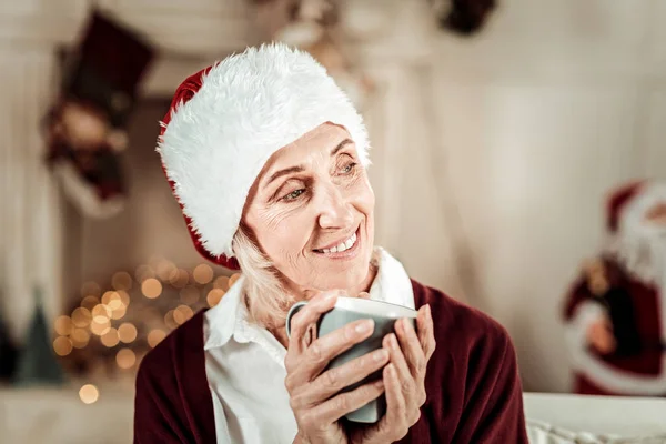 Mujer romántica satisfecha mirando a un lado y sosteniendo una taza . — Foto de Stock