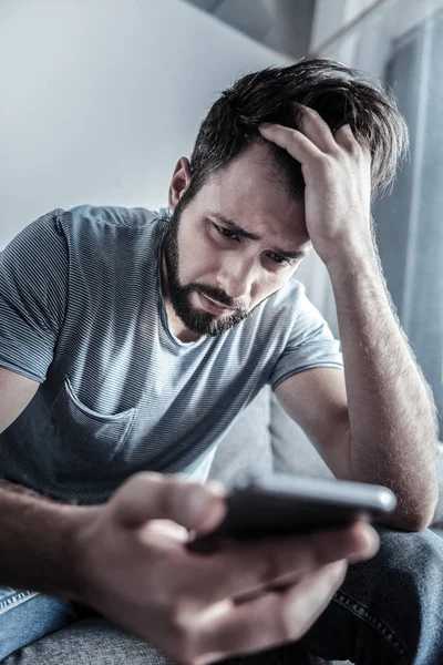 Want to cry. Disappointed young man bowing head and touching hair while reading negative message