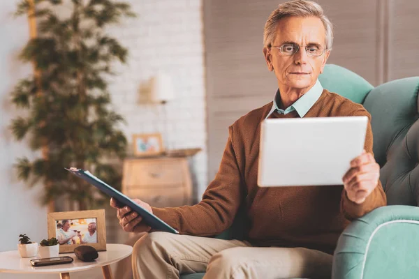 Pensionerad man som bär glasögon läsning månadsrapporter — Stockfoto