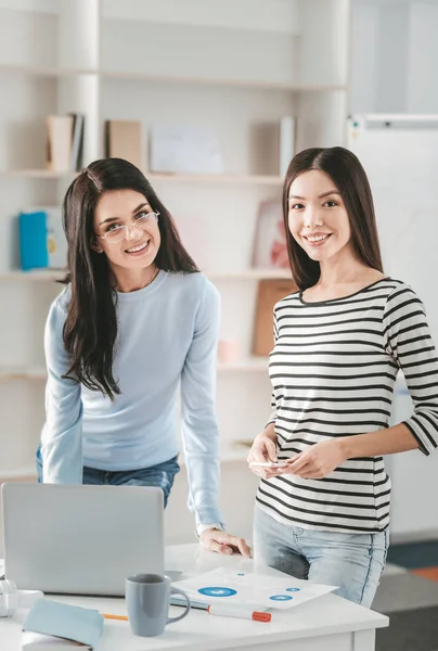 Two beaming dark-haired woman spending time in workspace — Stock Photo, Image