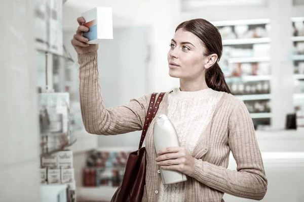 Клиент аптеки читает содержание витаминов после выбора шампуня — стоковое фото