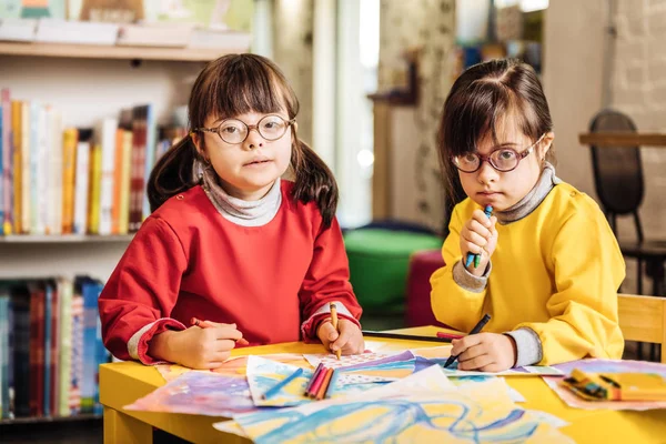 Schattige tweeling met syndroom van Down gevoel die betrokken zijn bij het kleuren foto 's — Stockfoto