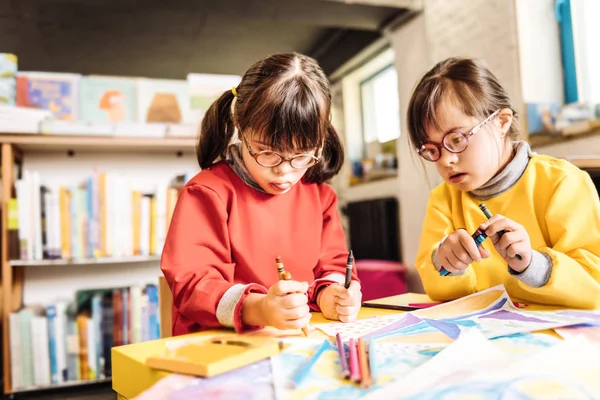 Funny sisters having Down syndrome holding crayons while drawing — Stock Photo, Image