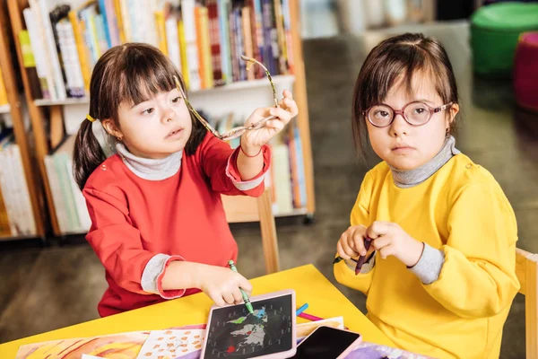 Girl with Down syndrome sitting near her sister taking glasses off — Stock Photo, Image