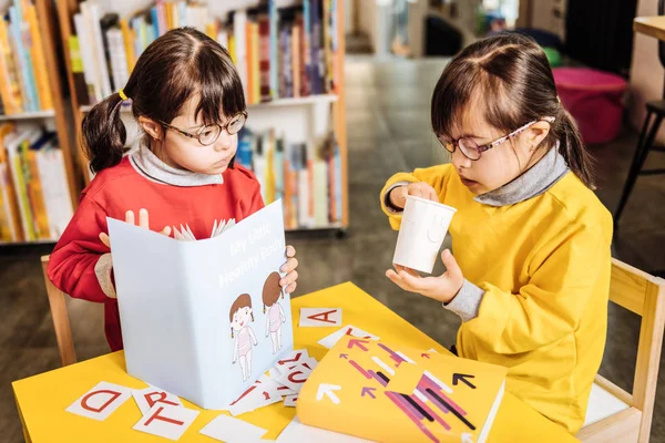 Sisters with genetic disorder wearing bright sweaters learning letters