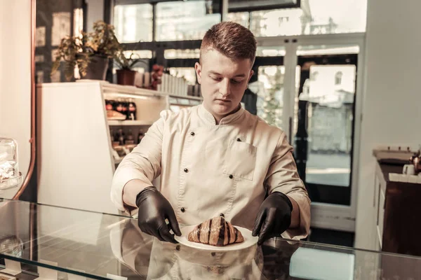 Netter professioneller Bäcker hält einen Teller mit Croissant — Stockfoto