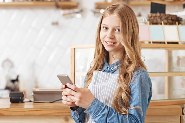 Barátságos kinézetű lány, smartphone, mosolyogva a kamerába — Stock Fotó